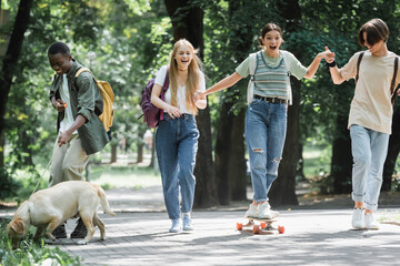 Interracial teenagers with retriever and skateboard having fun in park