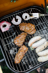 View of the grill with beef steaks, sausages and vegetables. meat and sausages are grilled on the grill. Spend time with your family at the grill. Social meetings, friends. Red grill with kindling
