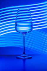 Crystal glass with pure water painted against the light-painted background. Studio shot, blue tones, surface reflections. Still life photos, beverages, glassware, backgrounds, glasses.