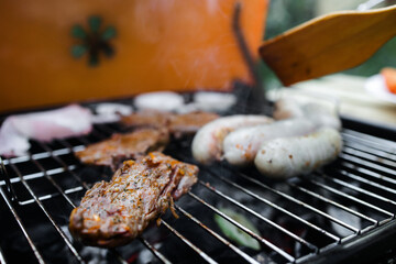 View of the grill with beef steaks, sausages and vegetables. meat and sausages are grilled on the grill. Spend time with your family at the grill. Social meetings, friends. Red grill with kindling