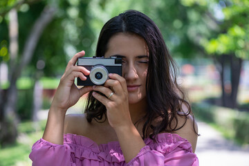 Woman in a pink dress taking photographs with a vintage film camera in a park