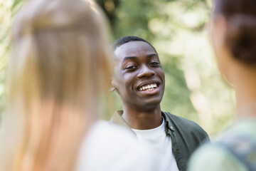 Smiling african american teenager looking at camera near blurred friends