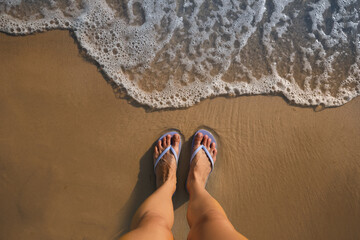 Top view of woman wearing beach slippers on sandy seashore, closeup