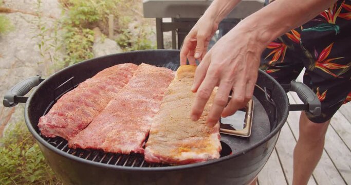 A rack of dry rubbed ribs being slow cooked and smoked on a kettle grill barbecue