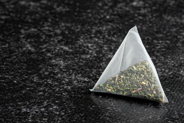 Pyramid tea bag with green tea lies on a dark vinyl textured kitchen background. Macro. Dark style