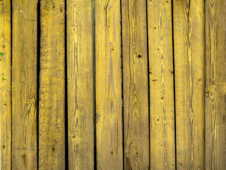 Old wooden fence made of boards painted with yellow paint.