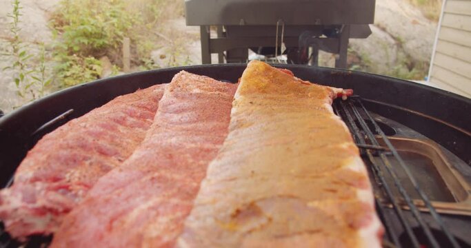 A rack of dry rubbed ribs being slow cooked and smoked on a kettle grill barbecue