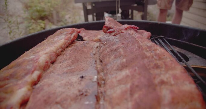 A rack of dry rubbed ribs being slow cooked and smoked on a kettle grill barbecue