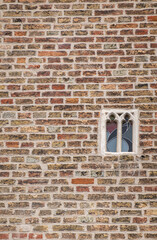 Brugge, Flanders, Belgium - August 4, 2021: Smallest spy window with stained glass in brown brick wall of Gruuthuse palace. 