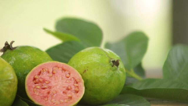 red pulp guavas on wooden table decorated with green leaves outdoors with blurred background