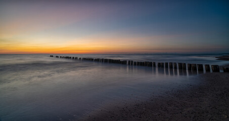 Fototapeta na wymiar long exposure of an ocean sunset with sandy beach and wooden pylon storm groin in the foreground
