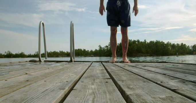 Adult male standing at the edge of a dock getting ready to backflip into the water