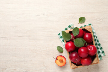 Delicious ripe cherry plums with leaves on white wooden table, flat lay. Space for text