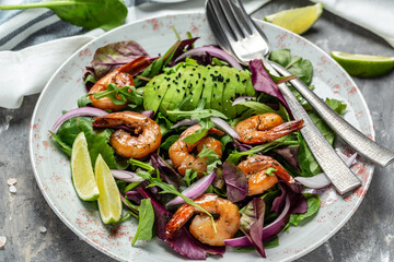 Green salad with avocado and shrimps salad. Seafood concept. Tasty veg mixed leaves, grilled prawn shrimps. Delicious breakfast or snack on a gray background, top view