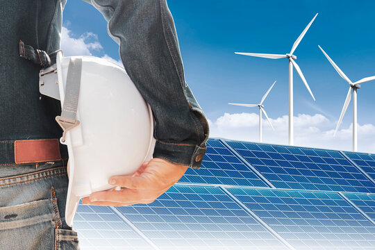 Engineer in jeans holding a white helmet in the construction site of wind turbines and solar power.