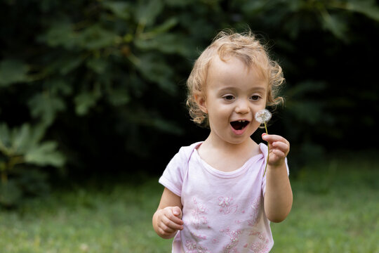 Baby girl blowing at dandelion in backyard