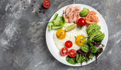 Ketogenic breakfast. Keto low carb salmon, boiled shrimps, prawns, fried eggs, fresh salad, tomatoes, cucumbers and avocado. Top view