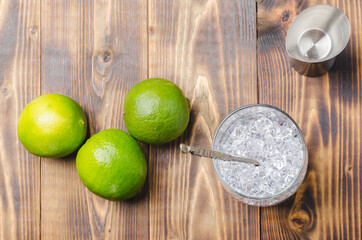 Ice for a cocktail and limes in glass on a wooden table.
