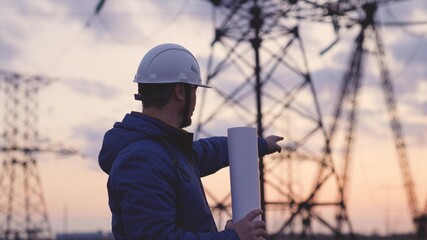 An electrician on the background of high towers of power plants looks at the project for the...