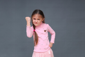 A little girl on a pink background threatens with a fist.