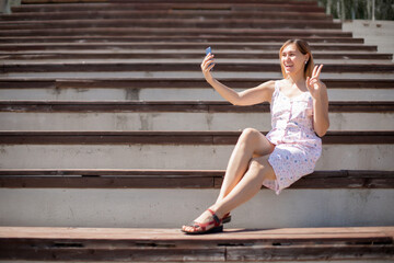 Fototapeta na wymiar Cute brunette girl taking selfie showing victory sign with hand in outdoors