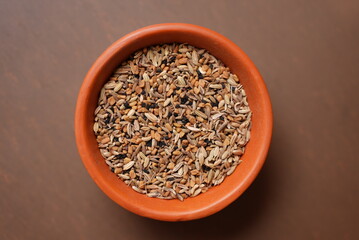 Some dry roasted Cumin seeds on a clay bowl on top of brown background