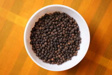 Some black paper grains on a clay bowl on top of yellow background texture