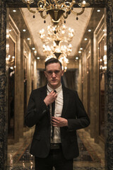 Portrait of young handsome business man in elegant business suit walking on the hall with beautiful expensive chandeliers. straightens his tie