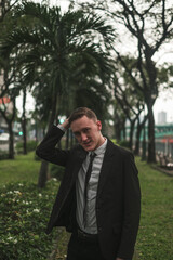 Portrait of handsome caucasian young entrepreneur in black formal suit outdoors. Looking at camera with copy space. Holding his head 