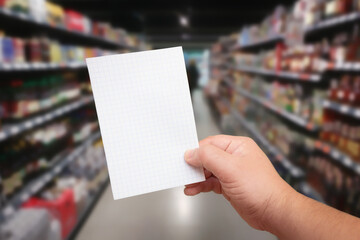 Paper for shopping list in hand at blurred background with supermarket aisle - 453152535