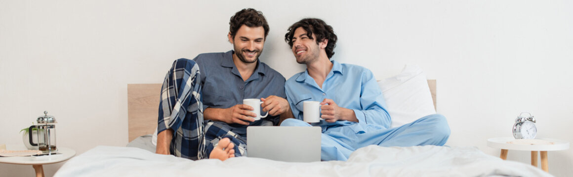 happy gay men watching movie on laptop and holding cups of tea, banner