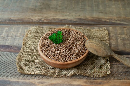 Organic buckwheat in a wooden bowl with a tablespoon and a sprig of parsley on a wooden table. Rustic style. Healthy nutrition concept. Buckwheat contains a large amount of vitamins and minerals.