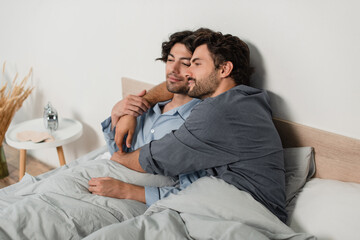 Fototapeta premium cheerful gay couple smiling while embracing in bed at home