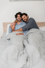 cheerful gay couple smiling while embracing in bed