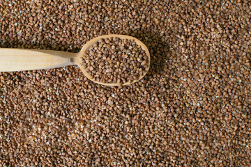 A wooden tablespoon lies on dry buckwheat, raw grains. Texture. Healthy nutrition concept. Horizontal orientation. Buckwheat contains a large amount of vitamins and minerals. Top view.