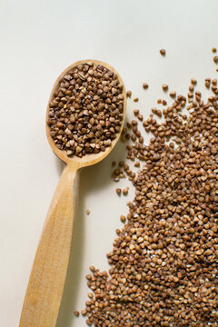 A wooden tablespoon lies with dry buckwheat and raw grains scattered on a light background. Healthy nutrition concept. Vertical orientation. Top view.