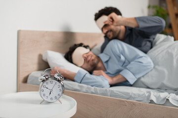 alarm clock on bedside table near blurred gay couple in eye masks
