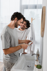 happy gay man looking at boyfriend squeezing toothpaste in bathroom