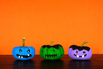 Painted Halloween pumpkins on a black shelf against an orange background. Monster, frankenstein and...