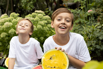 Two boys hold half of an unusual yellow watermelon and laugh in surprise. August is the watermelon season.