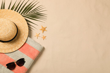Fototapeta na wymiar Beach towel, sunglasses, hat, palm leaf and starfishes on sand, flat lay. Space for text