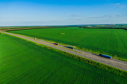 red green and blue trucks driving on asphalt road along the green fields and transported by container. seen from the air. Aerial view landscape. drone photography. cargo delivery