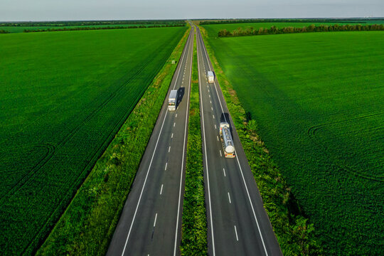 several trucks drive along the asphalt road along the green fields at sunset. seen from the air. Landscape from a bird's eye view. drone photo. delivery of cargo