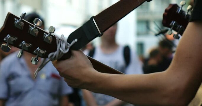A young street musician plays an acoustic guitar on a city street.