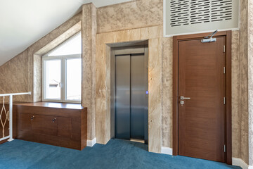 Interior of a carpeted hotel corridor with stainless steel lift door