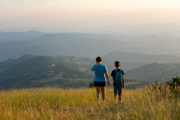 Fototapeta na wymiar family travel concept- mother and son hiking in mountains. Mother and Son enjoying the view after a mountain hike during sunset