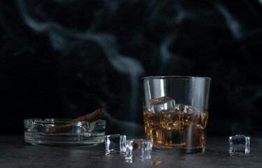 A glass of whiskey and ice cubes in clouds of blue smoke on a dark background