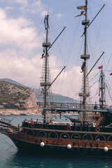 Vertical photo. Old pirate ship on the water of Mediteranean sea. Tourist entertainment, coastal tour. Summer sunny day. Mountain shore of Alanya. Turkey.