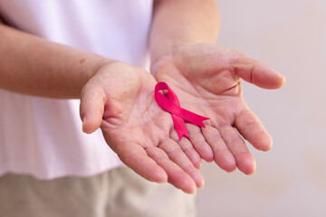 Focus on mature hand holding a pink ribbon isolated on white.