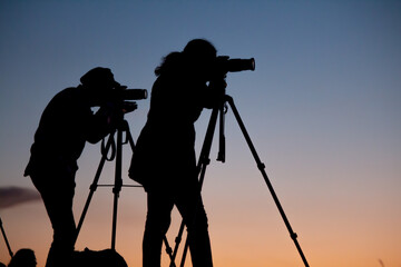 Siluetas  en el atardecer de artistas fotógrafos con sus cámaras y tripodes desde la montaña /...